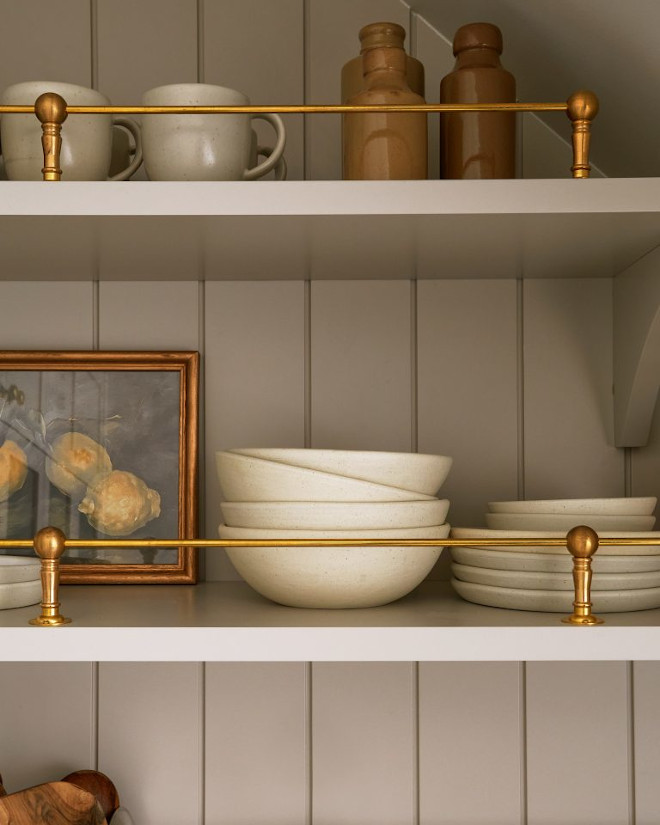Close-up of French country pantry shelves with aged brass railing, styled with ceramics and glassware, highlighting Benjamin Moore Revere Pewter cabinetry and timeless kitchen details.