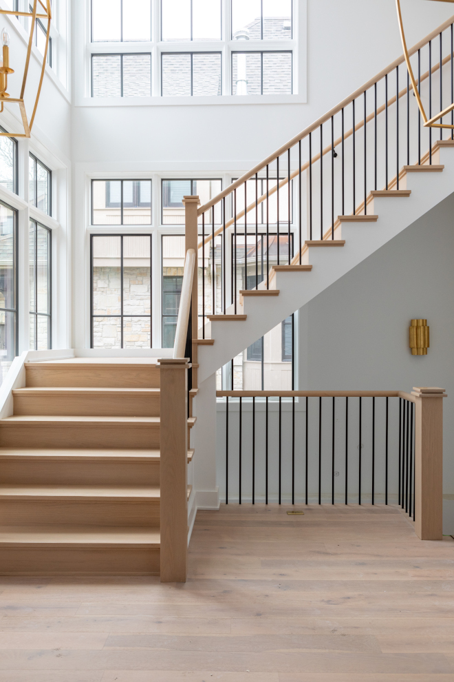 White oak staircase in a new construction home featuring custom stained treads, white oak newel posts, and satin black metal balusters under a two-story ceiling.