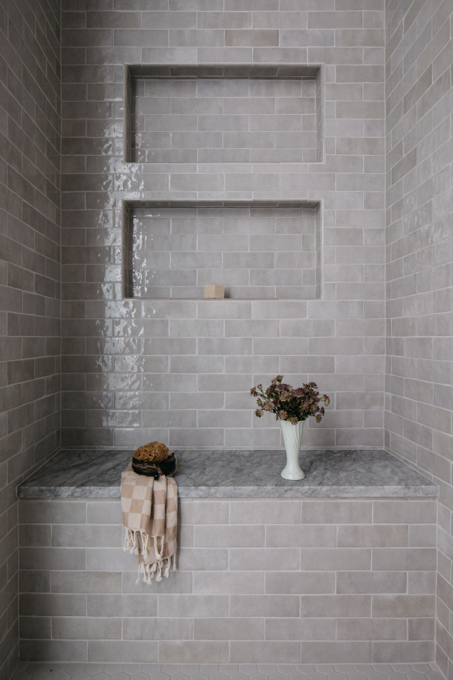 2026-new-home-bathroom-grey-textured-shower-marble-bench Shower with grey textured wall tiles, built-in niches, and Carrara White marble bench in a 2026 new construction home bathroom.