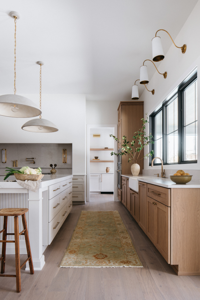 2026-new-home-kitchen-sink-wall-vanilla-milkshake-iron-ore-trim Kitchen sink area with perimeter cabinets, Benjamin Moore Vanilla Milkshake walls, Sherwin Williams Iron Ore window trim, pull-down faucet, and white brass sconces in a 2026 new build.