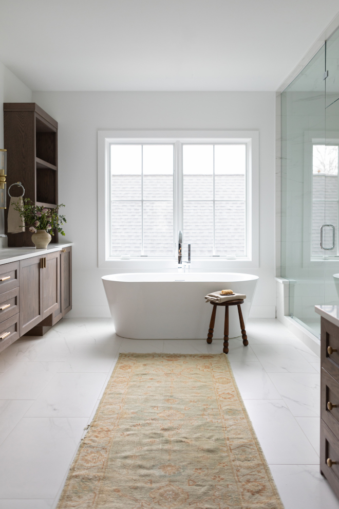 Primary bathroom painted Benjamin Moore Chantilly Lace with freestanding tub, tall windows, and marble-look porcelain floors.
