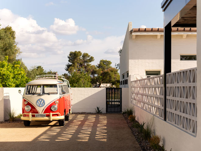 Curved driveway leading to a mid-century modern home with soft exterior colors and a red and white Volkswagen van parked nearby.
