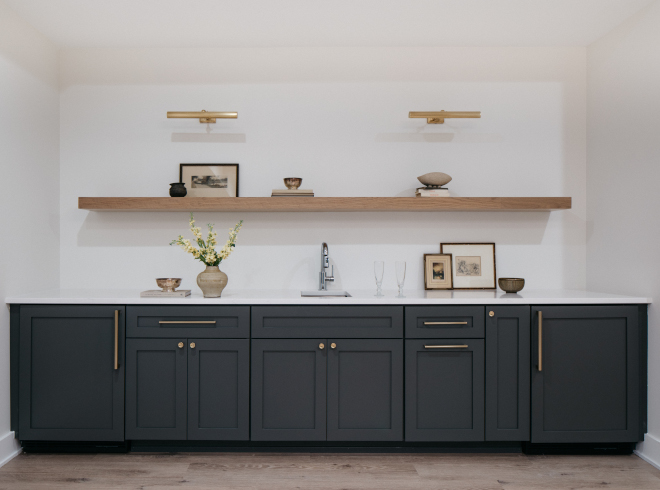 basement-bar-forged-steel-cabinets-vanilla-milkshake-walls Basement bar with cabinets painted Sherwin Williams Forged Steel, Vanilla Milkshake walls, floating shelf with picture lights, and MSI Calacatta Abezzo countertop.