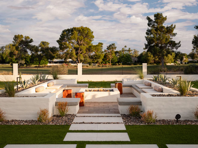 Backyard patio with built-in white seating walls and firepit, low planter beds, and mid-century modern design details.