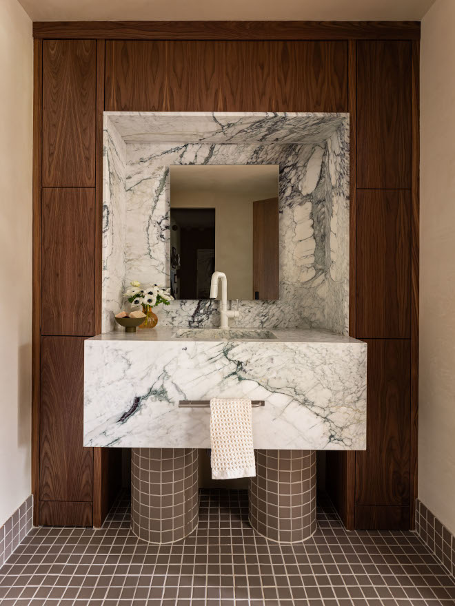 Compact mid-century modern hall bathroom featuring a sculptural floating vanity with Calacatta Vagli marble countertop, custom walnut cabinetry integrated into wall paneling, and textured tile vanity legs for a rich, layered design.