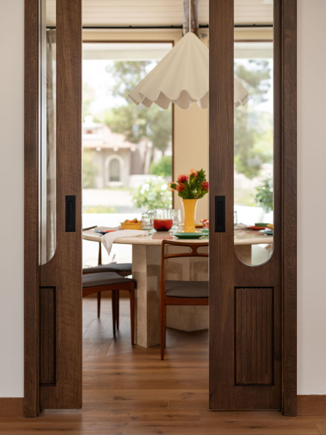 Custom walnut pocket doors with curved glass and reeded detailing leading to mid-century modern dining room.
