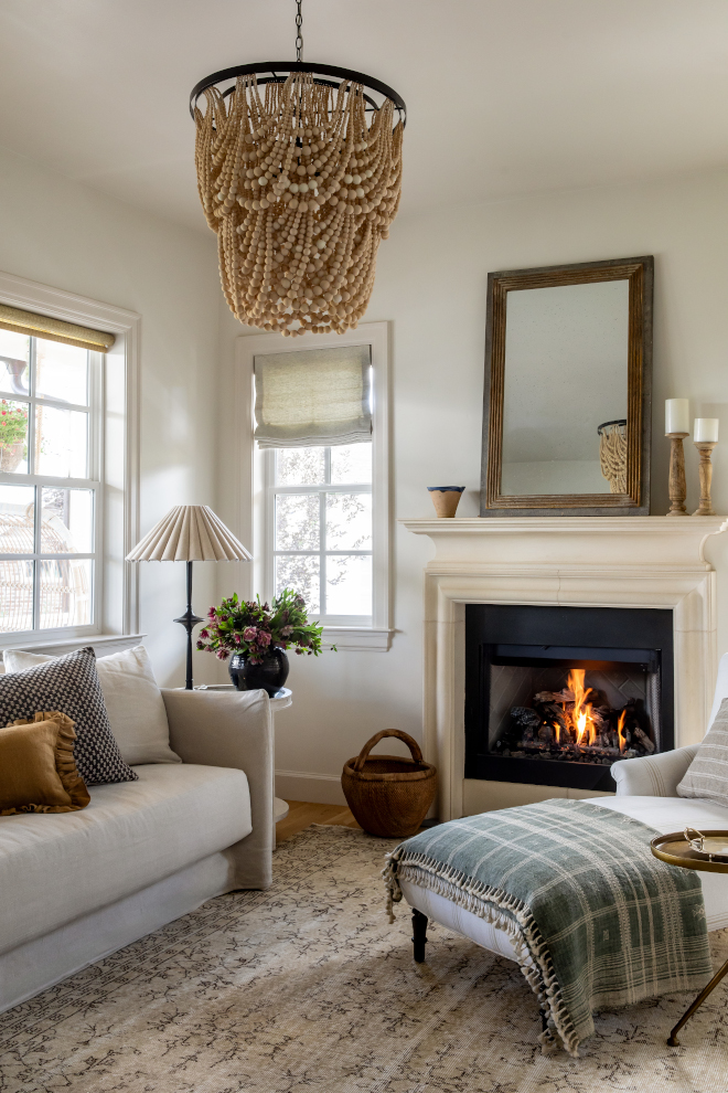 Living room painted in Benjamin Moore Swiss Coffee warm white, featuring cozy French Country style with cast stone fireplace, linen slipcovered sofa, draped wood bead chandelier, and layered neutral textures