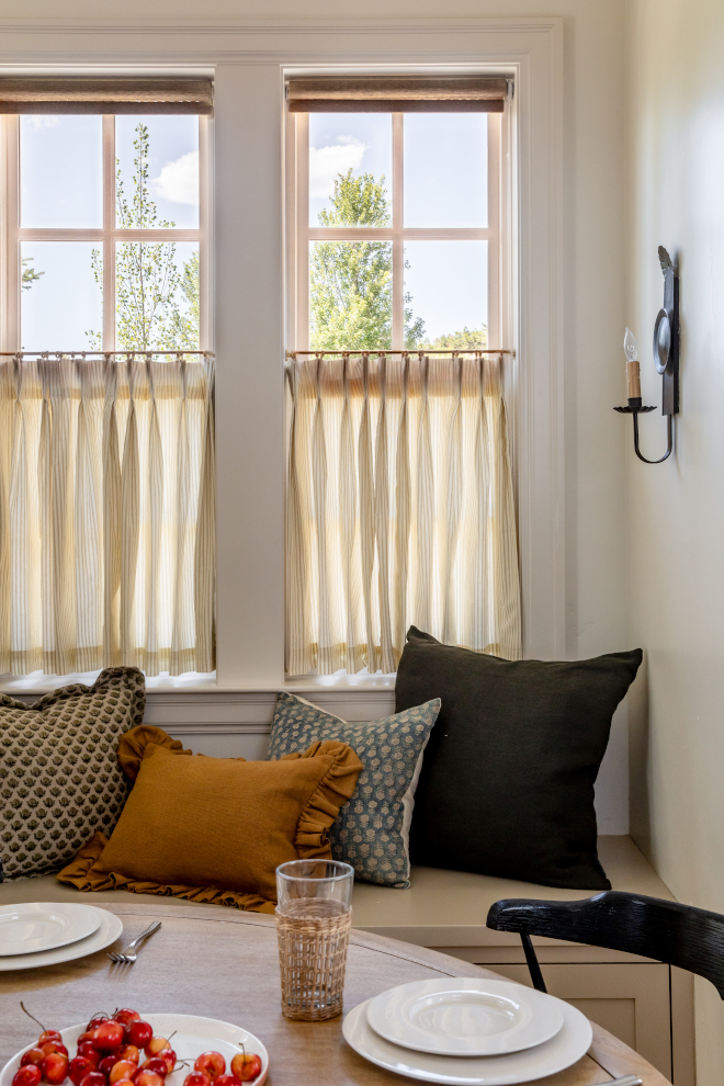Close-up of custom banquette tucked under windows with striped café curtains and designer pillows, French Country mountain home style