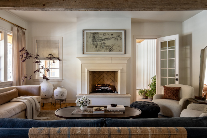 Family room in a mountain home featuring exposed ceiling beams, linen draperies, and a cast stone fireplace, exuding French Country warmth