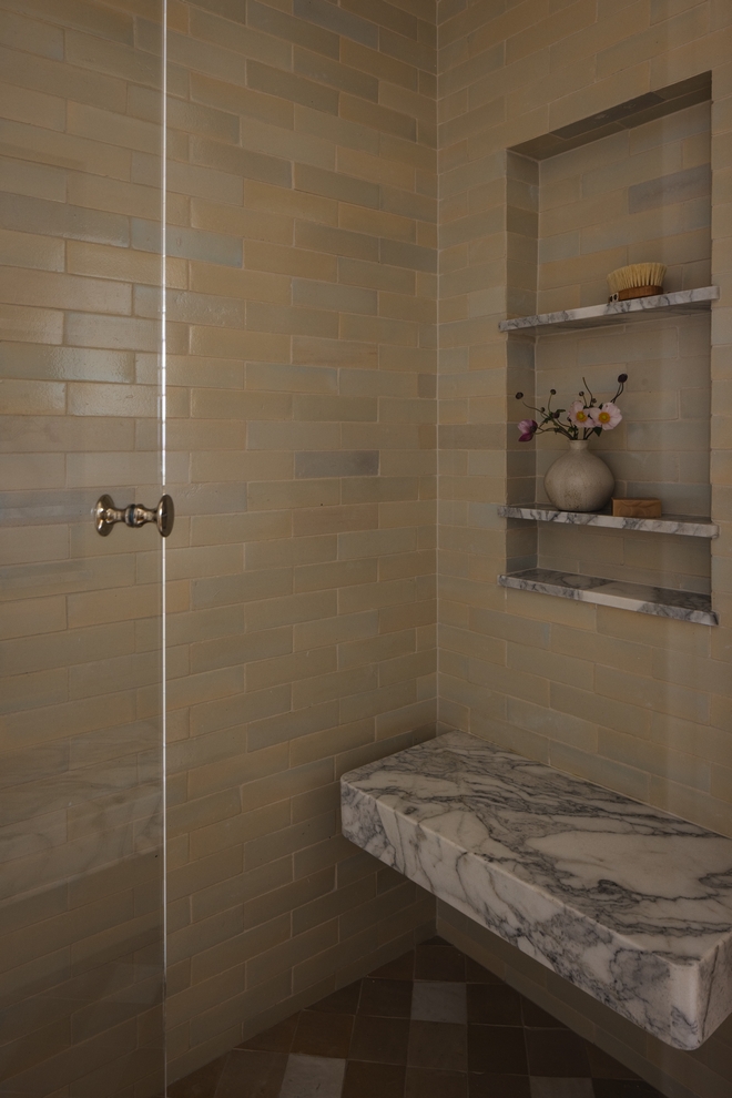 walk in shower with warm neutral tiles and marble bench with grey veining