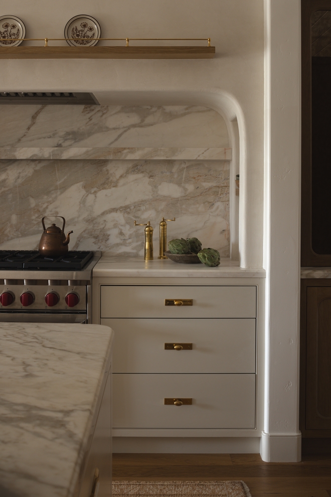 kitchen range alcove with rounded corners marble backsplash and Benjamin Moore Ballet White cabinetry with unlacquered brass hardware