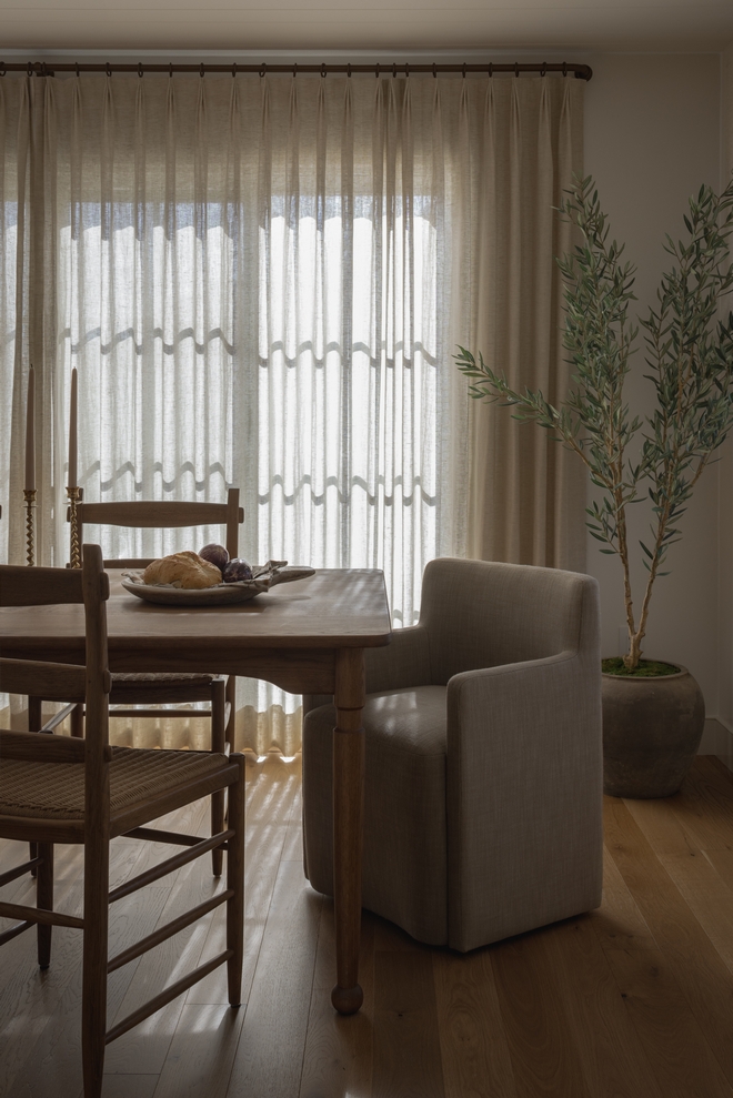 neutral dining room with oak dining table linen curtains and olive tree in vintage pot