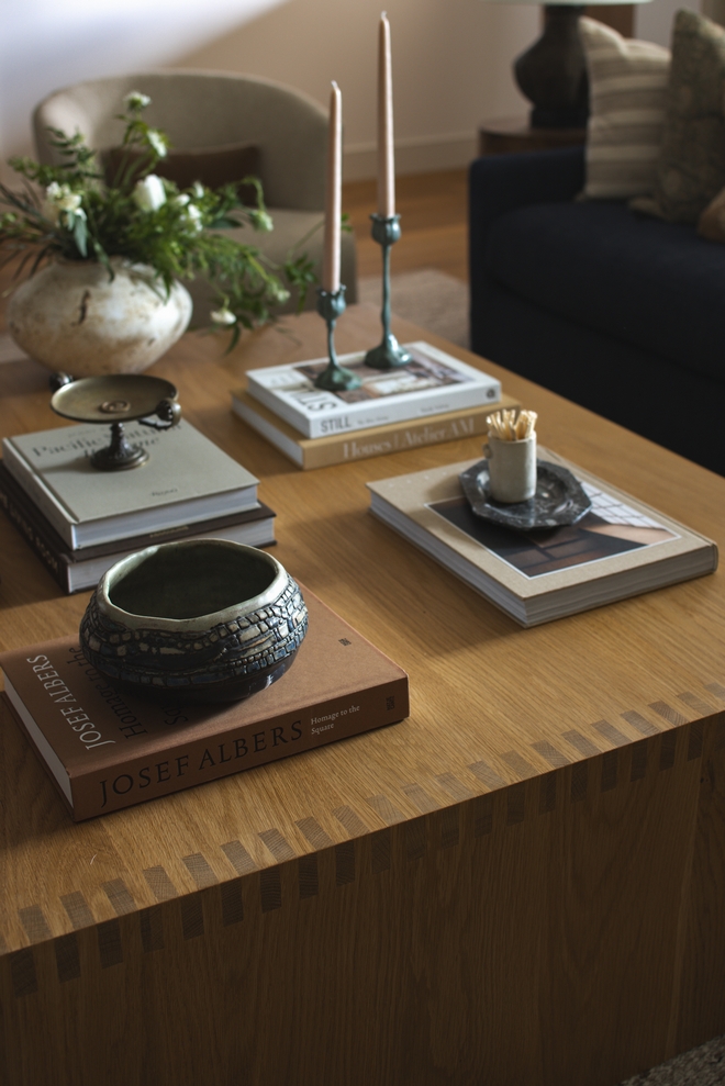 This beautifully crafted white oak waterfall coffee table features intricate box-joint detailing. Styled with antique accessories and design books, it adds craftsmanship and character to the relaxed living room.