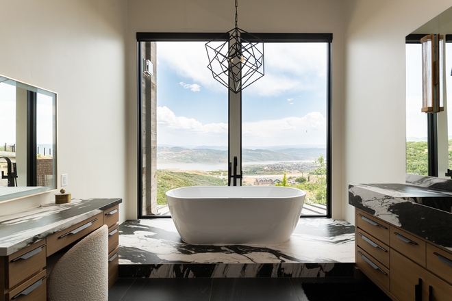 bathroom with freestanding tub in front of large window overlooking mountains and lake