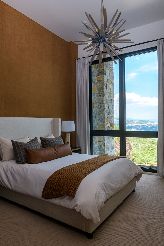 bedroom with warm tones, upholstered bed and large window overlooking mountains