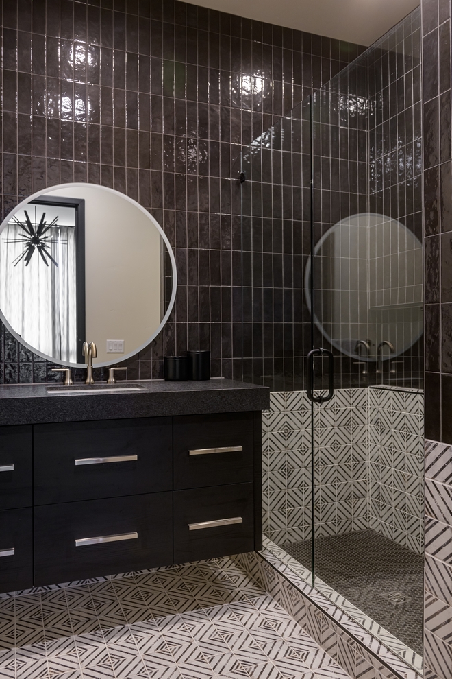 bathroom with dark tile walls, glass shower and round mirror