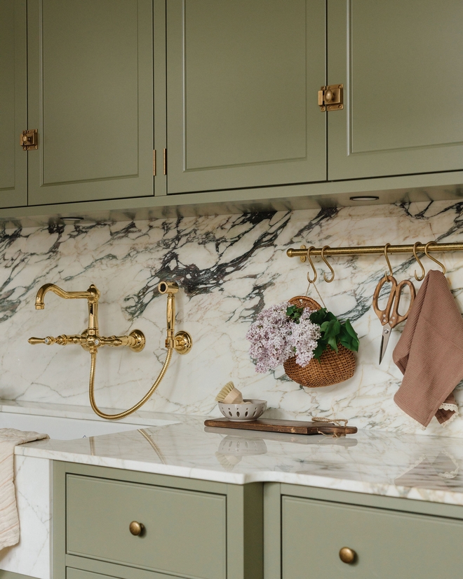 Kitchen with Benjamin Moore Louisburg Green cabinets, Calacatta Viola marble backsplash and countertops, and wall-mounted brass bridge faucet with hanging rail styling.