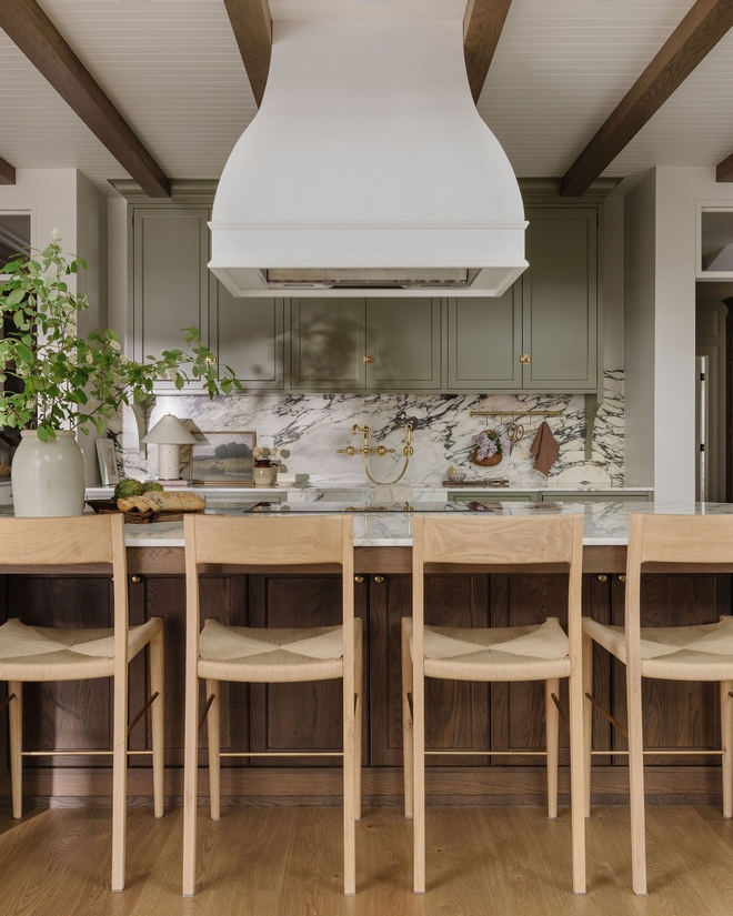 Balanced kitchen layout with green cabinetry, wood island, marble countertops, and bar seating in a warm organic modern space.