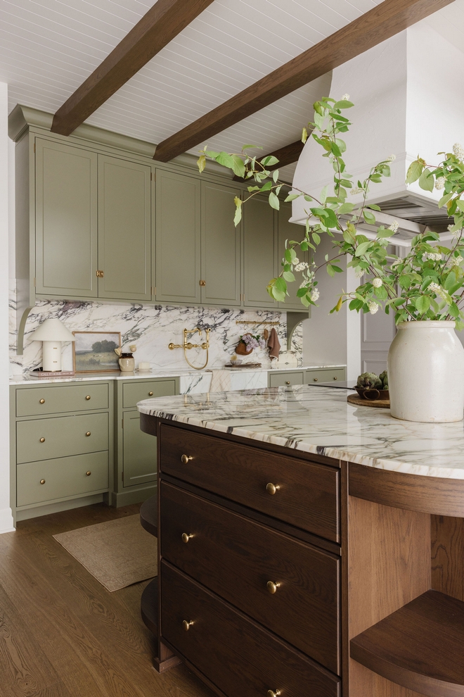 Detailed view of green kitchen cabinets with brass knobs, Calacatta Viola marble backsplash, and warm wood flooring.