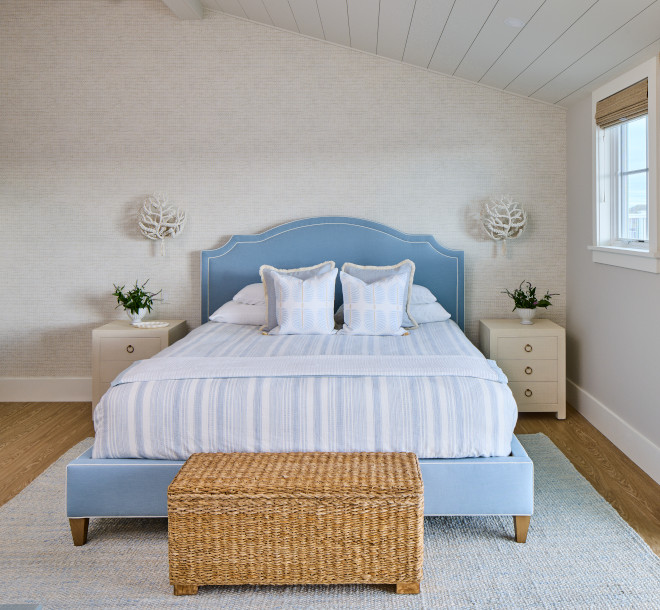 Coastal bedroom with pale blue bed, woven bench, and natural woven shades