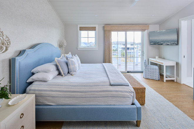 Coastal primary bedroom with soft blue upholstered bed, woven bench, and Sherwin Williams Drift of Mist walls