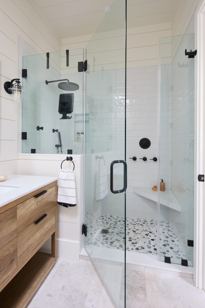 Coastal walk-in shower with white subway tile, pebble mosaic floor, and matte black fixtures