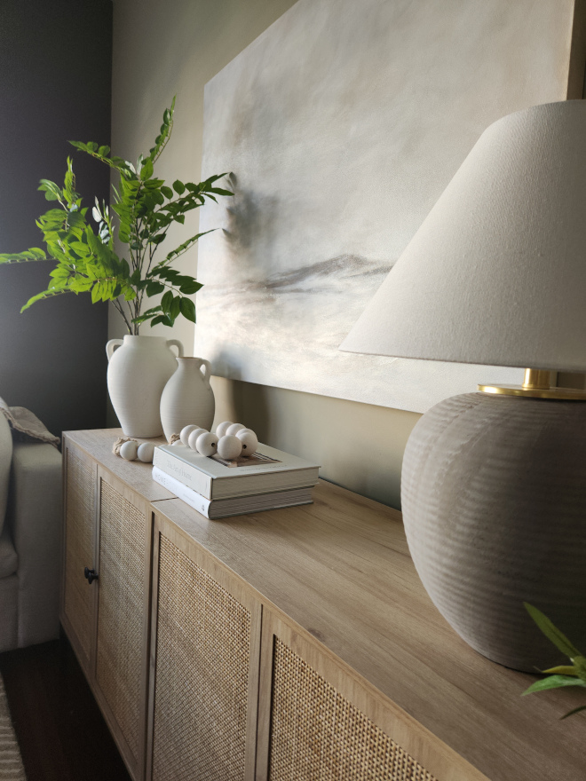 Warm wood cane cabinet styled with oversized artwork, textured lighting, greenery, and neutral decor in an earthy toned organic modern living room.