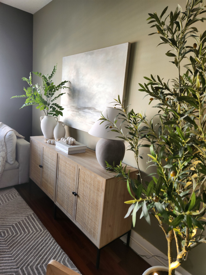 Earthy toned organic modern living room with warm neutral palette, black coffee table, woven cabinet, oversized artwork, greenery, and layered textures creating a custom designer look.