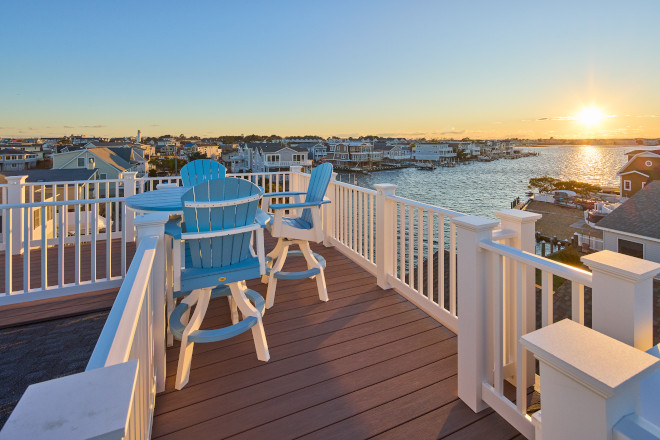 Rooftop coastal deck with blue Adirondack chairs overlooking the water at sunset.