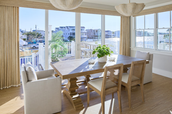 Coastal dining room with natural wood dining table, woven chairs, and waterfront windows