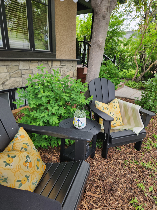 Outdoor seating area featuring white Adirondack chairs, floral arrangements, and sunny citrus accents in a charming front yard setting.