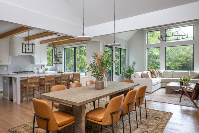 open-concept-kitchen-dining-living-room Open-concept kitchen, dining room, and living room featuring vaulted ceilings, exposed wood beams, large windows, woven counter stools, and warm leather dining chairs.