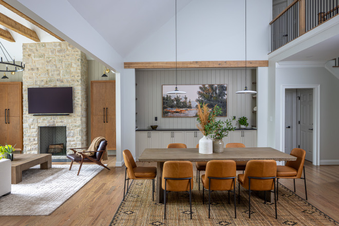 open-concept-living-dining-room-stone-fireplace Open-concept living and dining room featuring a floor-to-ceiling stone fireplace, custom built-ins, vaulted ceilings, exposed wood beams, and warm leather dining chairs.