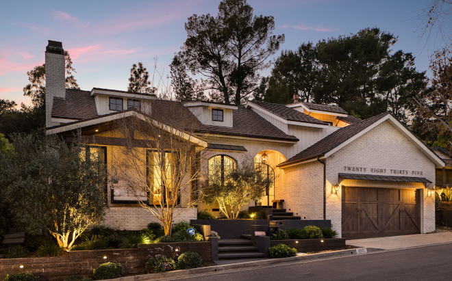 hollywood-hills-home-twilight-exterior-tour Twilight exterior of a remodeled Hollywood Hills home with limewashed brick, landscape lighting, timber accents, and warm interior glow.