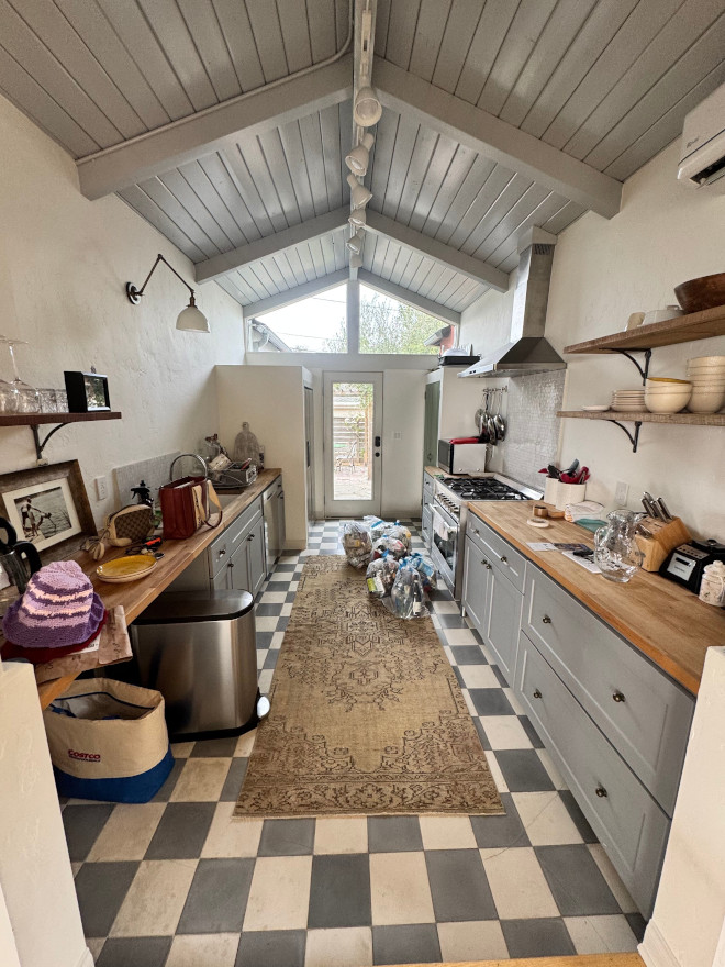 Narrow galley kitchen with a gray vaulted ceiling, wood counters along both walls, a patterned runner, and gray-and-white checkerboard flooring.