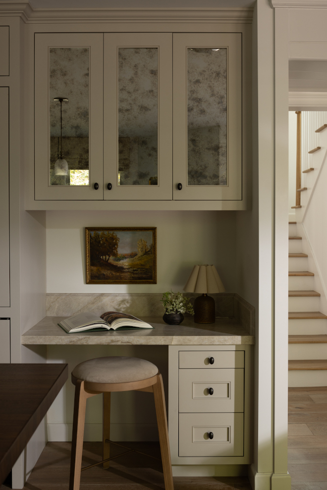 Built-in-English-Country-Kitchen-Desk Built-in taupe kitchen desk with antiqued mirror cabinets, stone worktop, vintage landscape art and upholstered wood stool.