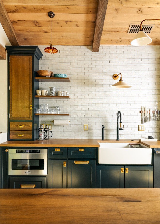 White Zellige backsplash behind open oak shelves and a farmhouse sink, paired with Hague Blue cabinets, brass hardware, and an oak ceiling.