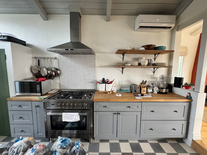 Kitchen before renovation with gray cabinets, wood countertops, open shelves, a stainless steel range, and checkerboard flooring.