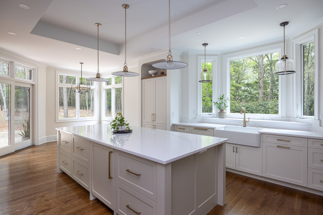Beautiful Classic White Kitchen Renovation with Large Island and Natural Light Timeless white kitchen with oversized quartz island, soft neutral Shaker cabinets, brass pendant lighting, warm hardwood floors, and large windows overlooking lush greenery.