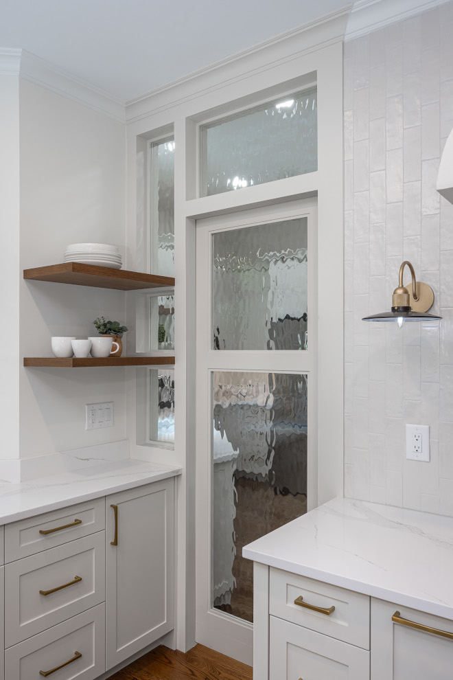 Pantry Door Ideas Closed Textured Glass Pocket Pantry Door Concealing Kitchen Pantry Fully closed white-framed pocket pantry door with decorative textured glass panels, concealing a secondary kitchen beside natural wood floating shelves and white ceramic tile.