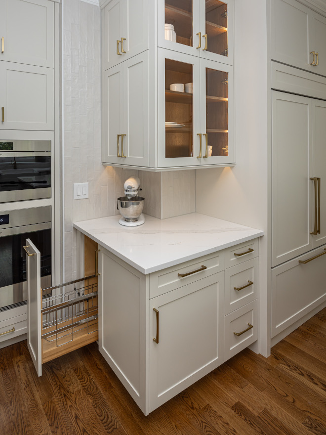Sherwin-Williams Slumber Sloth Cabinet Paint Color Sherwin-Williams Slumber Sloth Cabinet Paint Color Sherwin-Williams Slumber Sloth Shaker kitchen cabinets with illuminated glass-front display doors, warm wood interior shelves, brass pulls, and under-cabinet lighting above a white quartz countertop.