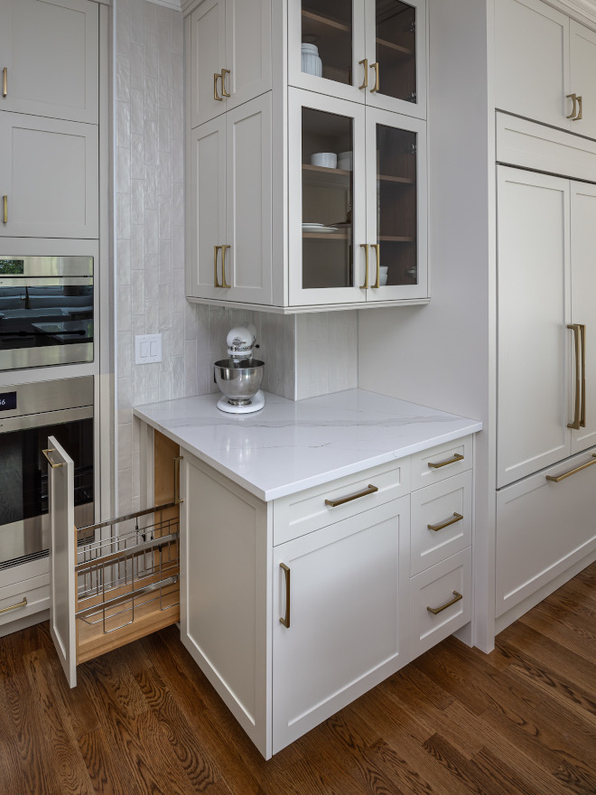 Smart Kitchen Storage Ideas with Pull-Out Cabinet Organizer Custom white kitchen cabinetry featuring a narrow pull-out wire storage organizer beside a countertop with a stand mixer, brass hardware, and glass-front upper cabinets.