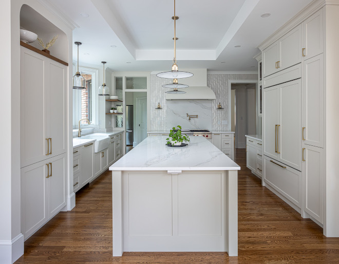 Timeless White Kitchen Renovation with Large Island and Brass Accents Beautiful North Carolina kitchen renovation featuring a large white island, warm hardwood floors, brass pendant lighting, white Shaker cabinets, and windows overlooking a wooded backyard.