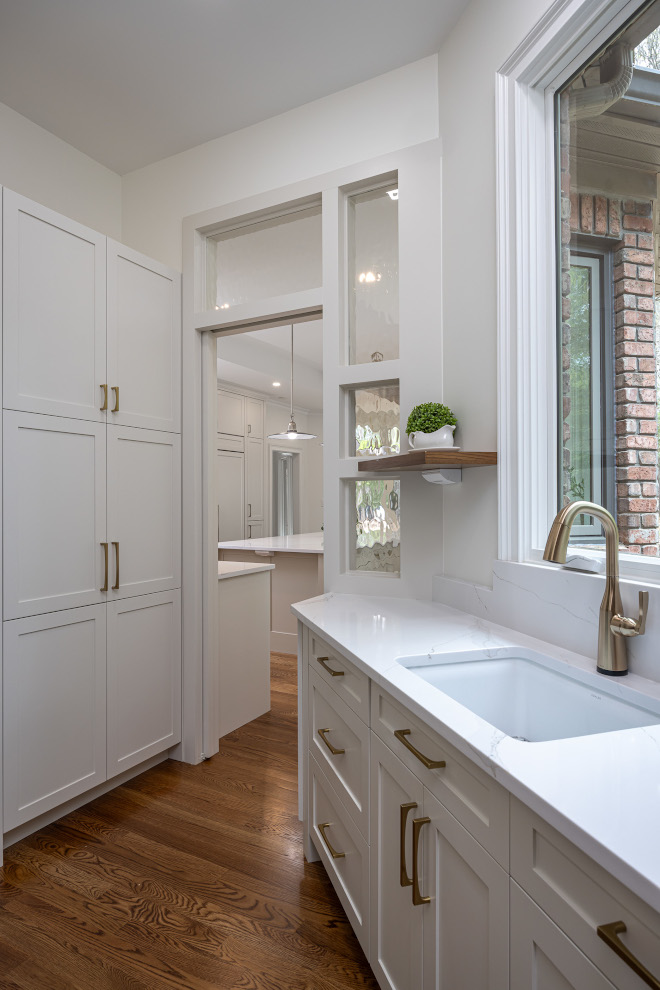 Walk-In Scullery with Custom White Cabinets and Textured Glass Details Secondary kitchen with white Shaker cabinets, brass hardware, undermount prep sink, white quartz countertops, and textured glass panels beside the doorway.