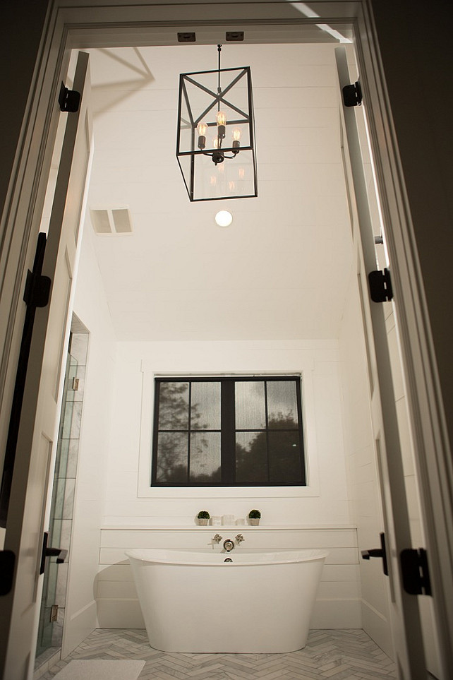 Bathroom Lighting. Gorgeous master bathroom features a freestanding tub placed in front of a built-in shiplap illuminated by a iron and glass lantern alongside a marble herringbone floor. #Bathroom #Lighting Hahn Builders.