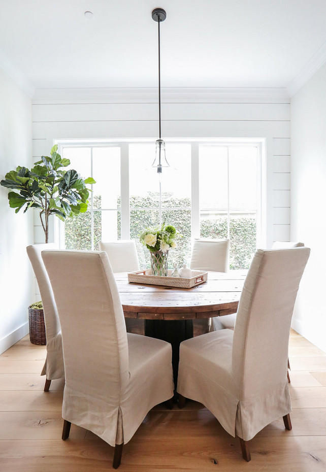 Breakfast Nook Table. Breakfast nook is lined with horizontal shiplap surrounding a round reclaimed wood dining table lined with natural linen slipcovered dining chairs illuminated by a clear glass pendant. The pendant is a Kichler Olde Bronze Everly Single-Bulb Indoor Pendant with Clear Glass Shade. #BreakfastNook #BreakfastNookTable