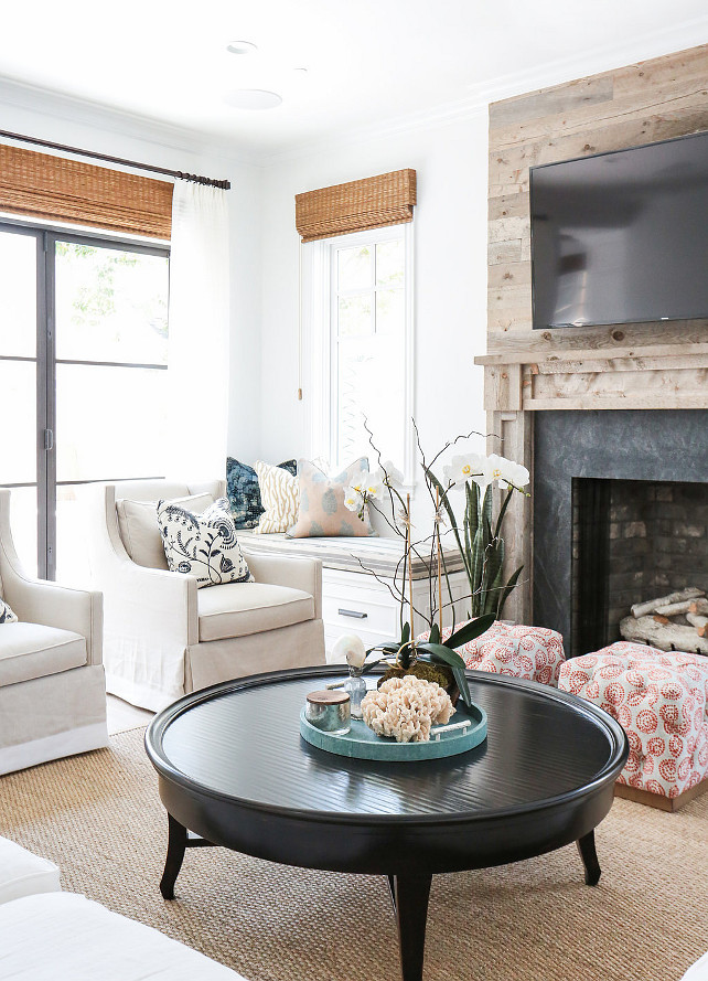 Living Room. Living Room features a plank fireplace mantle adorned with a black surround under a flatscreen TV flanked by built-in window seats accented with white and gray striped cushions. Living room is filled with a white sectional facing a round black coffee table and a pair of white curved chairs lined with black and white pillows. #LivinRoom Blackband Design.