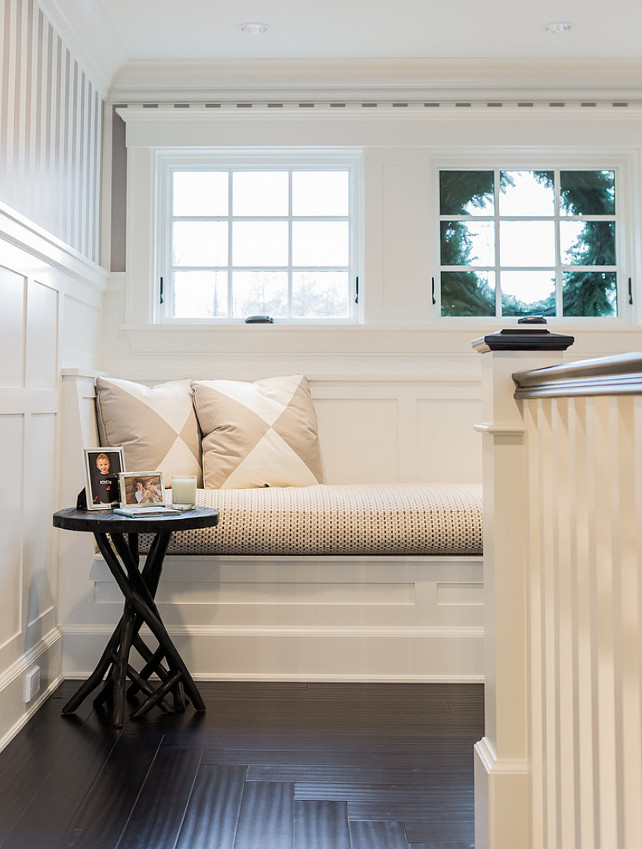 Staircase window seat - reading nook. Staircase reading nook. Staircase landing features a built-in reading nook topped with white and beige triangle pillows under windows framed by white and silver stripe wallpaper on upper walls and board and batten on lower walls alongside a branch accent table atop concentric wood floors. #Staircase #ReadingNook #WindowSeat Brookes and Hill Custom Builders. 