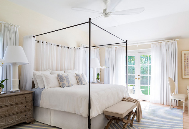 Master Bedroom. Coastal master bedroom. Master bedroom with oversized fan and iron canopy bed. White cotton linens, blue and white wool rug, linen upholstered bench and sheer drapery. Nightstands are substituted by large chests with oversized lamps which work well with the oversized scale of the bed and drapery. #masterbedroom #CoastalBedroom #CoastalMasterBedroom Chango & Co.