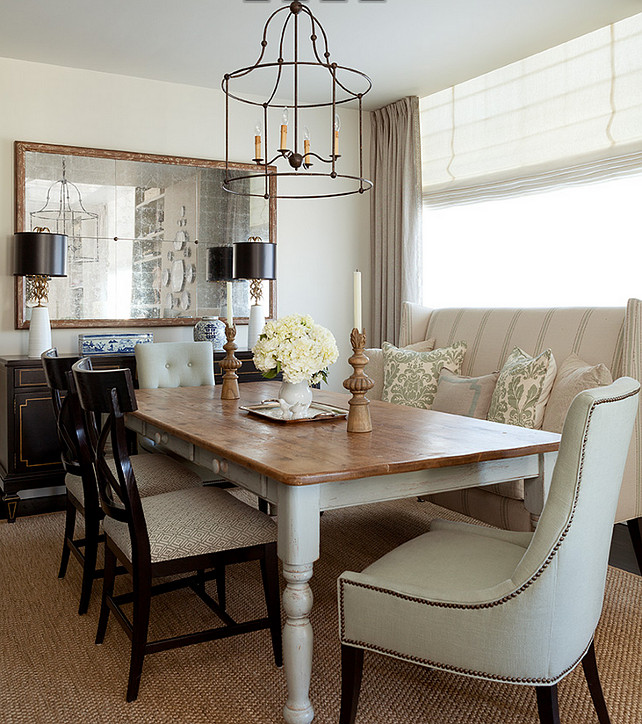 Dining Room. Traditional Dining Room. Traditional dining room features an iron cage chandelier illuminating a whitewashed farmhouse dining table lined with a striped wingback settee facing black x back dining chairs as well as button tufted dining chairs with brass tack trim. The back of the dining room boasts a black and gold buffet cabinet topped with white and gold lamps accented with black drum shades under a distressed mirror. #DiningRoom #Traditional #TraditionalDiningRoom Jenny Wolf Interiors.